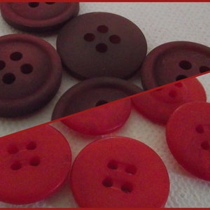 Peut inclure: Un assortiment de boutons dans des tons de rouge et de bordeaux. Les boutons sont ronds avec quatre trous chacun, et varient en taille et en finition. L'image est divisée en diagonale, avec des boutons plus foncés en haut et des boutons rouge vif en bas.