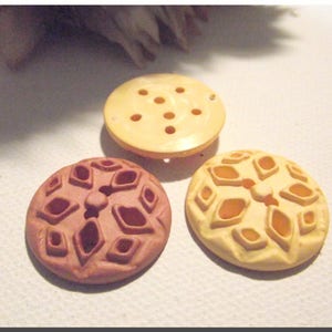 Könnte beinhalten: Drei dekorative Knöpfe mit komplizierten Designs. Die Knöpfe sind aus weißem, cremefarbenem und braunem Material gefertigt. Die Knöpfe haben ein erhabenes Design und sind perfekt, um jedem Projekt einen Hauch von Eleganz zu verleihen.