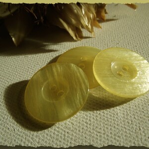 May include: Three yellow plastic buttons with four holes each. The buttons have a shiny, pearlescent finish.