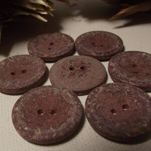 May include: Seven circular, reddish-brown buttons, each with two holes. The buttons display a textured surface and varying shades of brown, possibly made from a natural material. Suitable for sewing and craft activities.