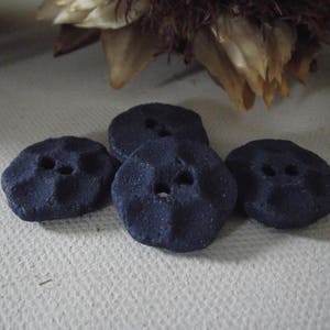 May include: Four dark blue ceramic buttons with two holes each. The buttons are slightly raised and have a textured surface.
