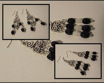 May include: Silver-toned chandelier earrings with black and white beads. The earrings have a decorative, swirling design and dangle with multiple strands of beads. The beads are oval-shaped and hang from the bottom of the earrings.