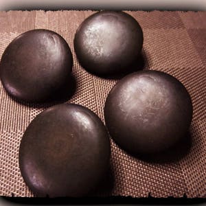 May include: Four dark brown, spherical objects with a slightly textured surface are arranged on a brown, patterned background. The spheres have a smooth, rounded shape and appear to be made of a solid material.