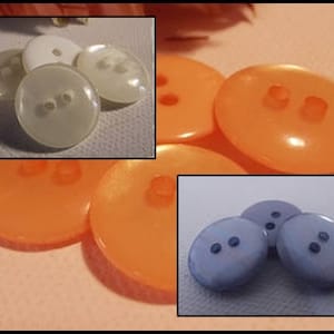 Könnte beinhalten: Eine Auswahl an ovalen Knöpfen in Orange, Weiß und Blau. Jeder Knopf hat zwei Löcher zum Annähen. Die Knöpfe sind in verschiedenen Größen erhältlich und eignen sich für Nähprojekte.