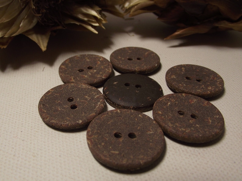 May include: Seven round, brown buttons with two holes each. The buttons are made of a textured material, with one button in a darker shade of brown. The buttons are arranged in a circular pattern.