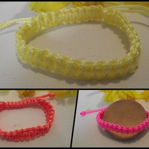 Puede incluir: Tres pulseras de macramé hechas a mano en amarillo, coral y rosa. Las pulseras son ajustables con nudos corredizos. La pulsera amarilla se muestra sobre una superficie blanca. Las pulseras coral y rosa se muestran sobre una superficie blanca y un objeto de madera.