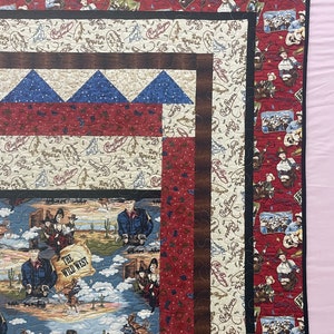 May include: A patchwork quilt featuring Roy Rogers themed fabric with western motifs. The design includes panels of cowboys, desert landscapes with cacti, and text reading The Wild West. The quilt is bordered by red and cream patterned fabric.