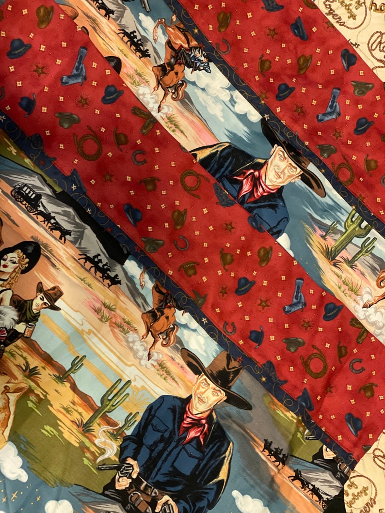 May include: A fabric featuring a Western theme with repeating diagonal panels. One panel displays cowboys, cacti, and desert landscapes, while the alternating red panel is patterned with small brown cowboy hats, lassos, and gold stars.