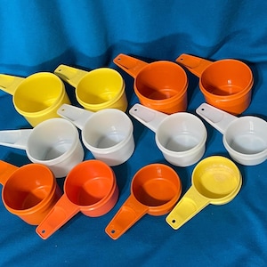 May include: A collection of colorful measuring scoops in yellow, orange, and white. Each scoop has a handle and a rounded bowl. The scoops are arranged on a blue surface, creating a visually appealing display.