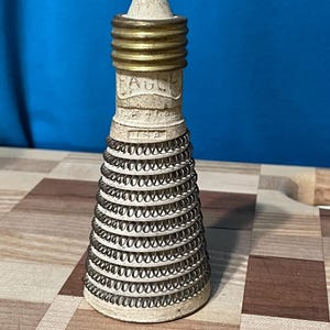 May include: A vintage bottle stopper with a cream-colored base and a brass-colored top. The stopper has a spiral wire design around the base and the word "EAGLE" is printed on the side. The stopper is marked "USA".