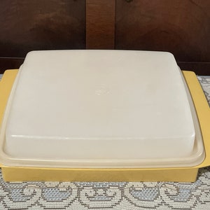 May include: A yellow plastic serving tray with a clear lid. The tray has a square shape and is made of a durable plastic.