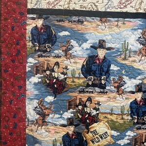May include: A quilted fabric featuring a Wild West theme with repeating illustrations of Roy Rogers, cowboys, and cowgirls in desert landscapes. The design includes cacti, horses, and a scroll with the text THE WILD WEST, bordered by a red patterned strip.