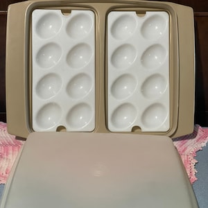 May include: A beige plastic egg cooker with a clear lid. The cooker has two sections, each with six egg-shaped molds.