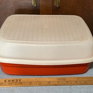 May include: A red plastic food storage container with a white lid. The lid has a grid pattern and the words "Sears" printed on it.