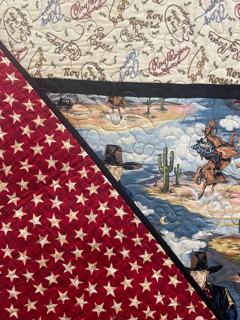 May include: A quilted fabric featuring a red section with a repeating pattern of beige stars and a black border separating it from a desert scene with cowboys on horseback, cacti, and mountains, plus a top section with Roy Rogers text.