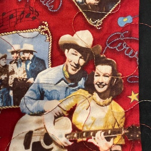 May include: A red fabric featuring a vintage-style print of a cowboy and cowgirl playing a guitar, with additional imagery of musical notes, a rope-bordered photo of people in cowboy hats, and the embroidered text Happy Trails in blue thread.