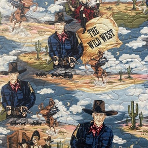 May include: A quilted fabric featuring a Wild West theme with illustrations of cowboys in dark blue shirts and red neckerchiefs, saloon performers, horses, cacti, and desert landscapes. The text THE WILD WEST is printed on a parchment-style scroll.