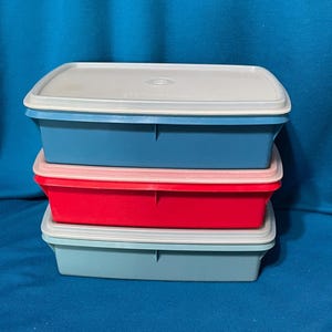 May include: Stack of three rectangular food storage containers in blue, red, and light blue. Each container has a matching lid in a light gray color. The containers are made of plastic and are designed for food storage.