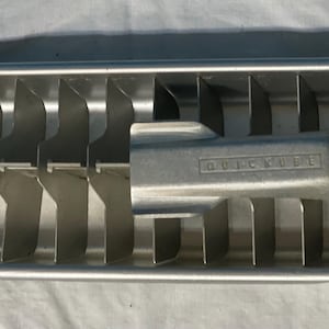 May include: A silver metal ice cube tray with 12 compartments. The tray has the words "Quick Cube" embossed on the side.