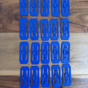 May include: Twenty blue plastic buckles with a rounded rectangular shape and three small circles on each buckle.