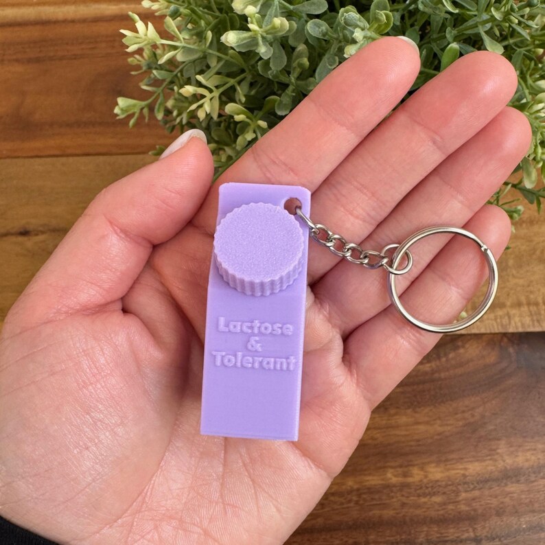 Op de afbeelding: Een paarse sleutelhanger in de vorm van een melkpak met de tekst "Lactose & Tolerant".