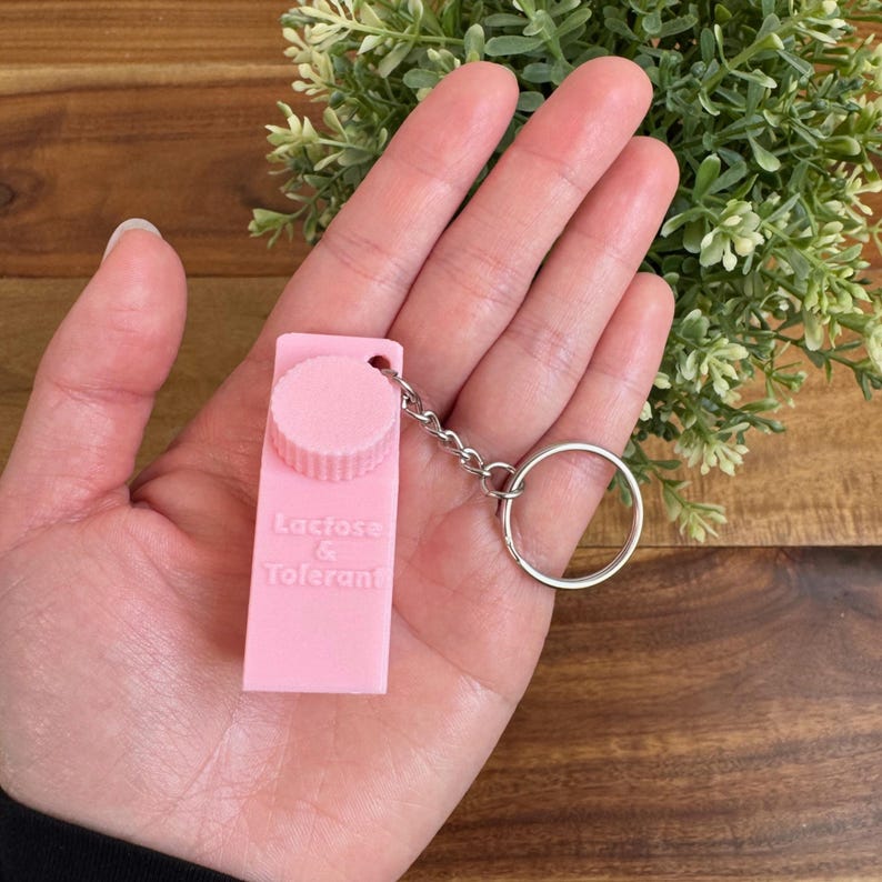 Op de afbeelding: Roze plastic sleutelhanger in de vorm van een melkpak met een wit schroefdeksel. De sleutelhanger heeft de tekst "Lactose & Tolerant" op de voorkant.