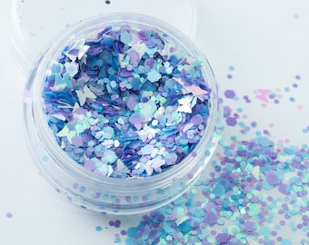 May include: A clear jar filled with iridescent blue and purple glitter. The glitter is scattered around the jar on a white surface.