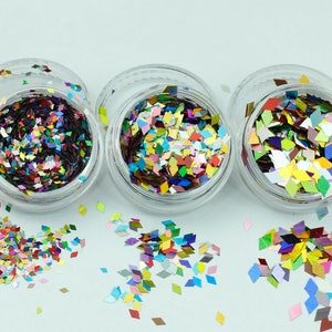 May include: Three small jars filled with colourful diamond-shaped glitter. The glitter is a mix of iridescent and opaque colours, including red, green, blue, gold, and silver.
