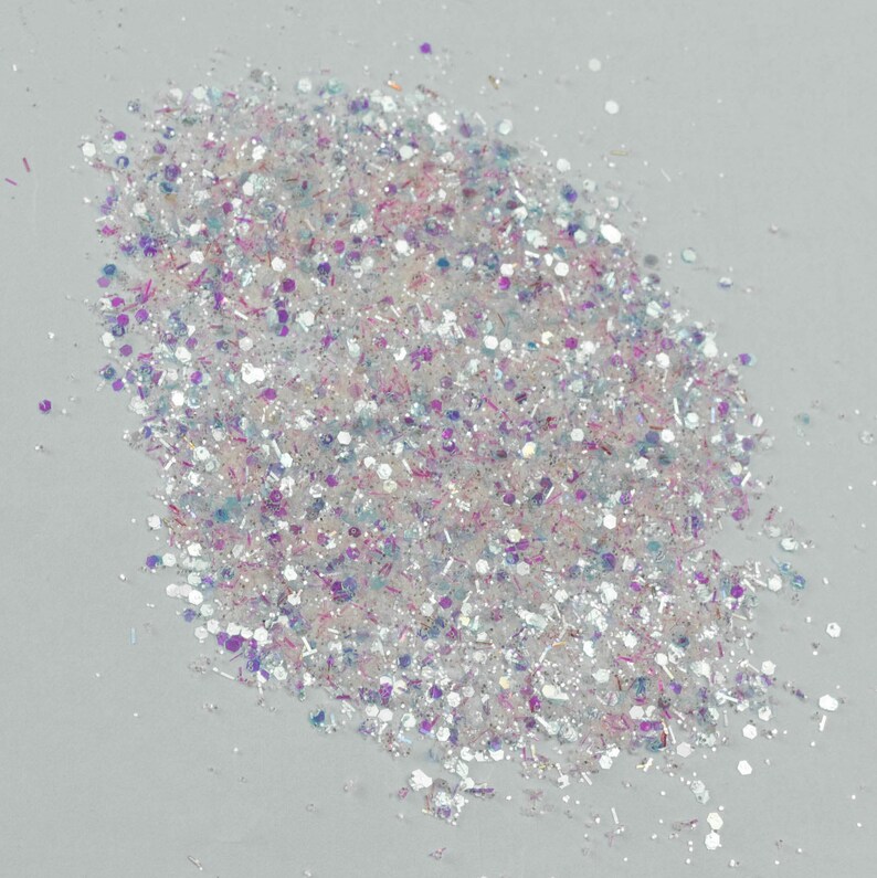 Puede incluir: Un mont&oacute;n de purpurina iridiscente con una mezcla de formas y tama&ntilde;os. La purpurina presenta una mezcla de tonos blancos, plateados, rosas, morados y azules. Las part&iacute;culas reflectantes brillan, creando un efecto brillante, ideal para manualidades y decoraciones.
