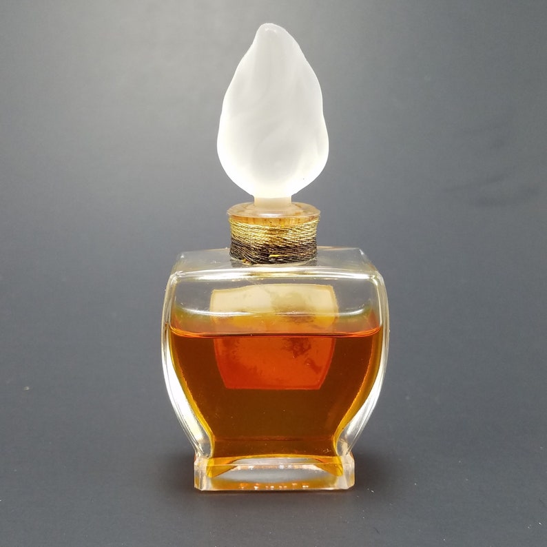 May include: A clear glass bottle with a brown liquid inside. The bottle has a unique, leaf-shaped stopper made of frosted glass.