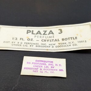May include: Two white labels with black text for Plaza 3 perfume. The top label reads "Plaza 3 Perfume 1/2 fl. oz. - Crystal Bottle Dist. by G Perfumes, Inc. New York, N.Y. 10012 Under Lic. by Bergdorf & Goodman Co.". The bottom label reads "Distributor BG Perfumes, Inc. N.Y. Under Lic. by Bergdorf & Goodman Co. Net 1/4 fl. oz."