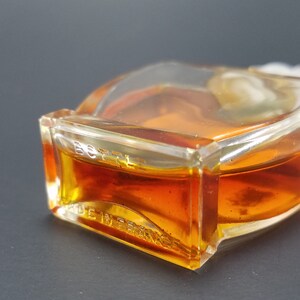 May include: A clear glass bottle with a gold liquid inside. The bottle has a textured surface and the words "BOTTL  MADE IN FRANCE" are printed on the bottom.
