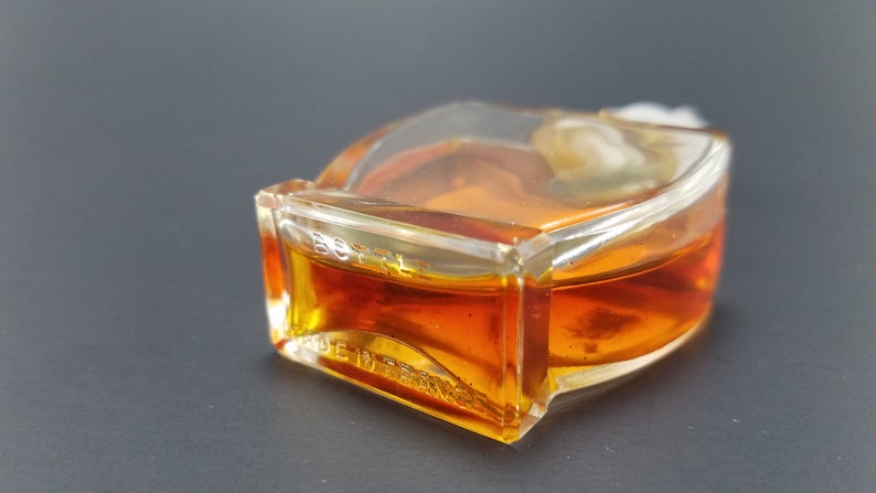 May include: A clear glass bottle with a gold liquid inside. The bottle has a textured surface and the words "BOTTL  MADE IN FRANCE" are printed on the bottom.