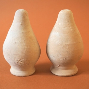 Peut inclure: Deux objets en céramique blanc cassé en forme de poire, à surface texturée. Chacun a une base arrondie et un sommet plus étroit. Les objets sont présentés sur un fond orange, suggérant un thème de poterie ou de décoration intérieure.