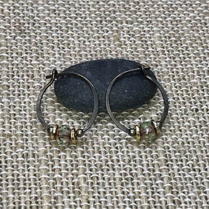 May include: A pair of hoop earrings with a small, green and gold bead on each hoop.