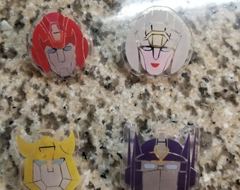 Może przedstawiać: Cztery przezroczyste breloki z różnymi postaciami Transformersów. Postacie to Optimus Prime, Megatron, Starscream i Arcee. Breloki są w różnych kolorach: Optimus Prime jest czerwony, Megatron fioletowy, Starscream żółty, a Arcee biały.