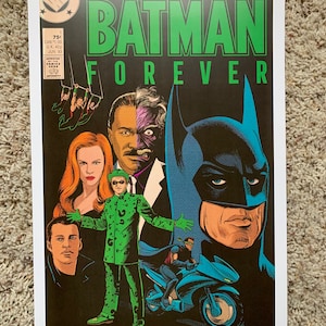 May include: A vintage comic book cover for Batman Forever, featuring a dark background with Batman, Two-Face, Catwoman, and The Riddler. The cover is green, blue, and black with the title "Batman Forever" in large green letters.