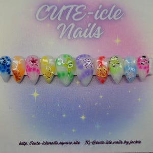 May include: A set of ten almond-shaped false nails with a variety of colorful designs. Each nail features a different color gradient and floral or abstract patterns. The nails are arranged on a gradient background with the text "CUTE-icle Nails".
