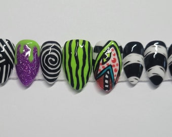 May include: A collection of ten false fingernails, each with a different Halloween design. The nails showcase a variety of colours, such as neon green, purple glitter, black and white stripes, and mummy bandages. Each nail has a unique design.