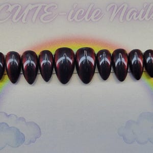 May include: Set of ten oval-shaped false nails. Each nail is a deep burgundy color with a white and red design. The nails are arranged on a clear plastic strip against a background with a rainbow and clouds. The text "CUTE-icle Nails" is at the top.