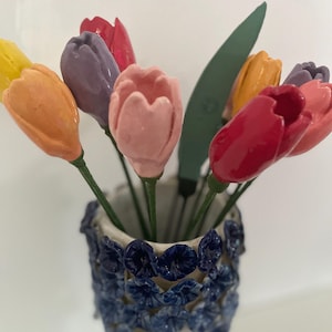 May include: A bouquet of colourful ceramic tulips in a blue and white ceramic vase. The tulips are in shades of pink, red, purple, orange and yellow.