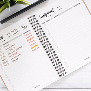 May include: A close-up of a spiral bound planner with a brown cover. The planner is open to a page with a list of assignments and due dates. The page is titled "Assignment Tracker" and includes a section for class, assignment, due date and time. The planner is on a white surface.