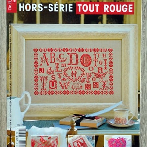 Peut inclure: Couverture du magazine "De fil en aiguille Hors-série n°18" avec le sous-titre "TOUT ROUGE". La couverture présente un sampler au point de croix rouge encadré avec l'alphabet. Autres éléments : un petit pichet, une tasse de thé et un livre.