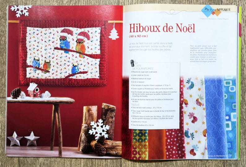 Op de afbeelding: Een boek met een rode kaft en een kleurrijk quiltontwerp van uilen op een tak. Het boek is open op een pagina met instructies voor het maken van de quilt. De tekst op de pagina luidt "Hiboux de No&euml;l (60 x 82 cm)".