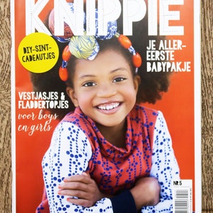 May include: A magazine cover featuring a young girl wearing a red and white patterned shirt with blue polka dots. The magazine is titled "KnipPie" and has the text "DIY-SINT-CADEAUTJES" and "JE ALLER-EERSTE BABYPAKJE" on the cover. The magazine is for sizes 50 to 176.