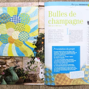 May include: A colorful quilt with a pattern of circles and stripes. The quilt is made of fabric scraps in shades of yellow, blue, and green. The quilt is titled "Bubbles de champagne" and is 30 inches by 30 inches.