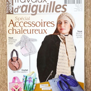 Könnte beinhalten: Ein Magazincover mit einer Frau, die eine beige Strickmütze und einen Schal trägt. Das Magazin heißt "travaux d'aiguilles" und der Titel auf dem Cover lautet "Spécial Accessoires chaleureux". Das Cover zeigt verschiedene gestrickte und gehäkelte Artikel, darunter eine Mütze, ein Schal, eine Tasche und Hausschuhe.