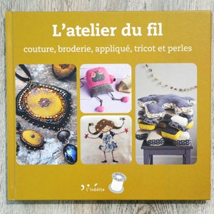 以下が含まれることがあります： 「L'atelier du fil」というタイトルと「couture, broderie, appliqué, tricot et perles」というテキストが書かれた黄色の本の表紙。表紙には、ビーズネックレス、ピンクのフェルトのおもちゃ、布の正方形の積み重ね、そして長い髪の女の子の画像が掲載されています。