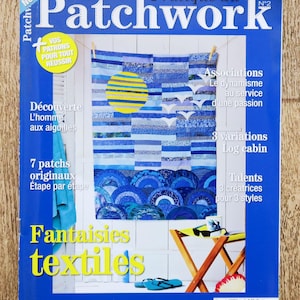 Può includere: Una copertina di rivista intitolata Pratique du Patchwork n. 2 che mostra una trapunta blu con un sole giallo e sagome di uccelli bianchi. La copertina include testo, uno sgabello pieghevole in legno, un paio di infradito blu e una tazza.