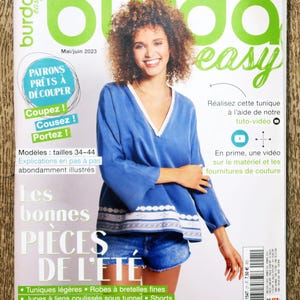 Puede incluir: La portada de la revista Burda Easy, número 3/2023, presenta a una mujer sonriente con una blusa azul y pantalones cortos de mezclilla. La portada de la revista tiene el texto "Les bonnes PIECES DE L'ETE" y "PATRONS PRÊTS À DÉCOUPER".